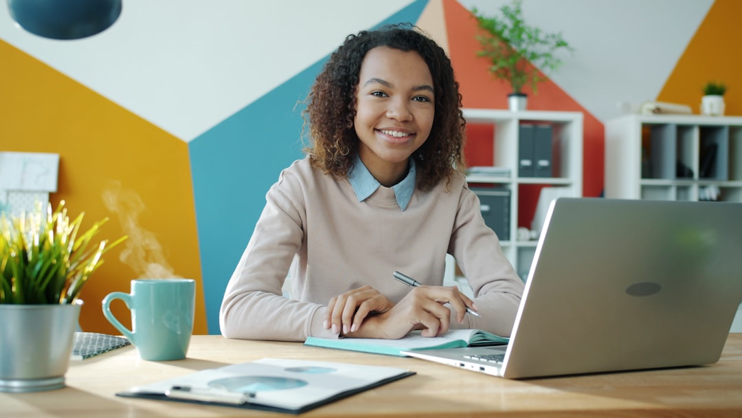 A professionally dressed person smiles with relief and success while looking at their laptop, symbolizing passing the real estate exam.